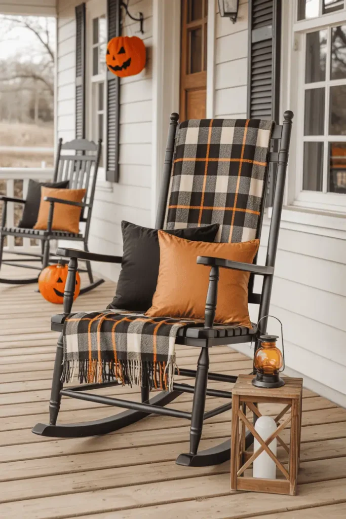 Farmhouse rocking chair with plaid throw, orange cushions, and rustic wooden lantern beside it for Halloween porch setup.