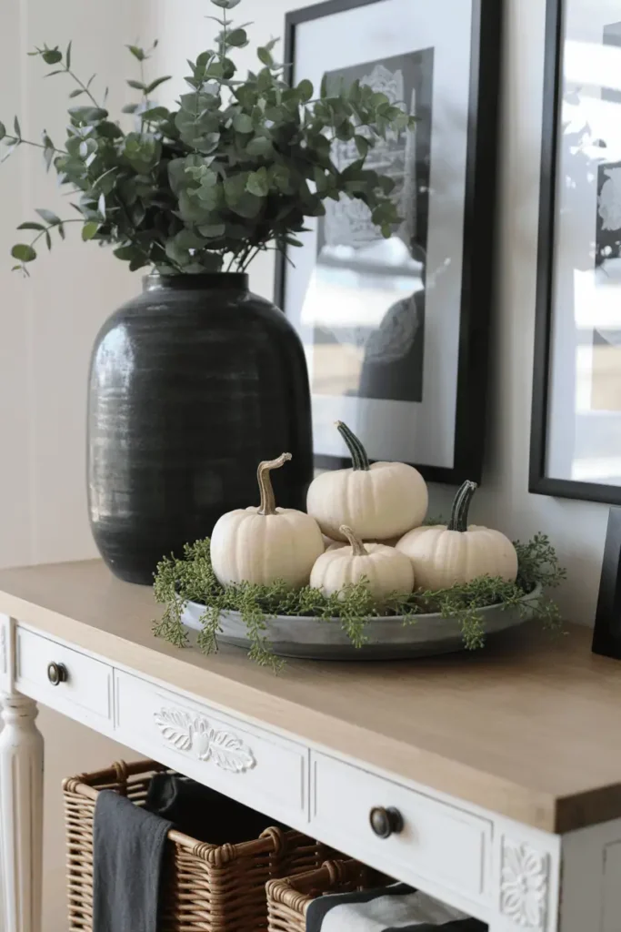 Neutral farmhouse console with black vase and pumpkins.